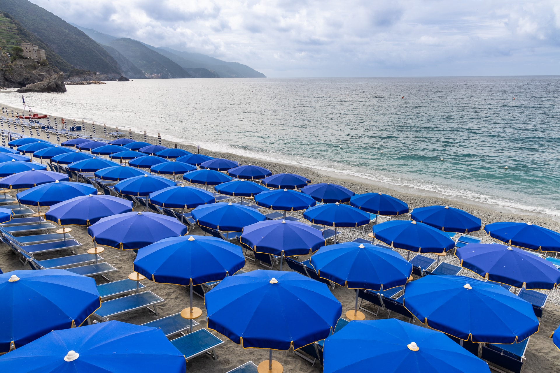 file di ombrelloni blu su una spiaggia ligure in estate - vacanze-marine.it
